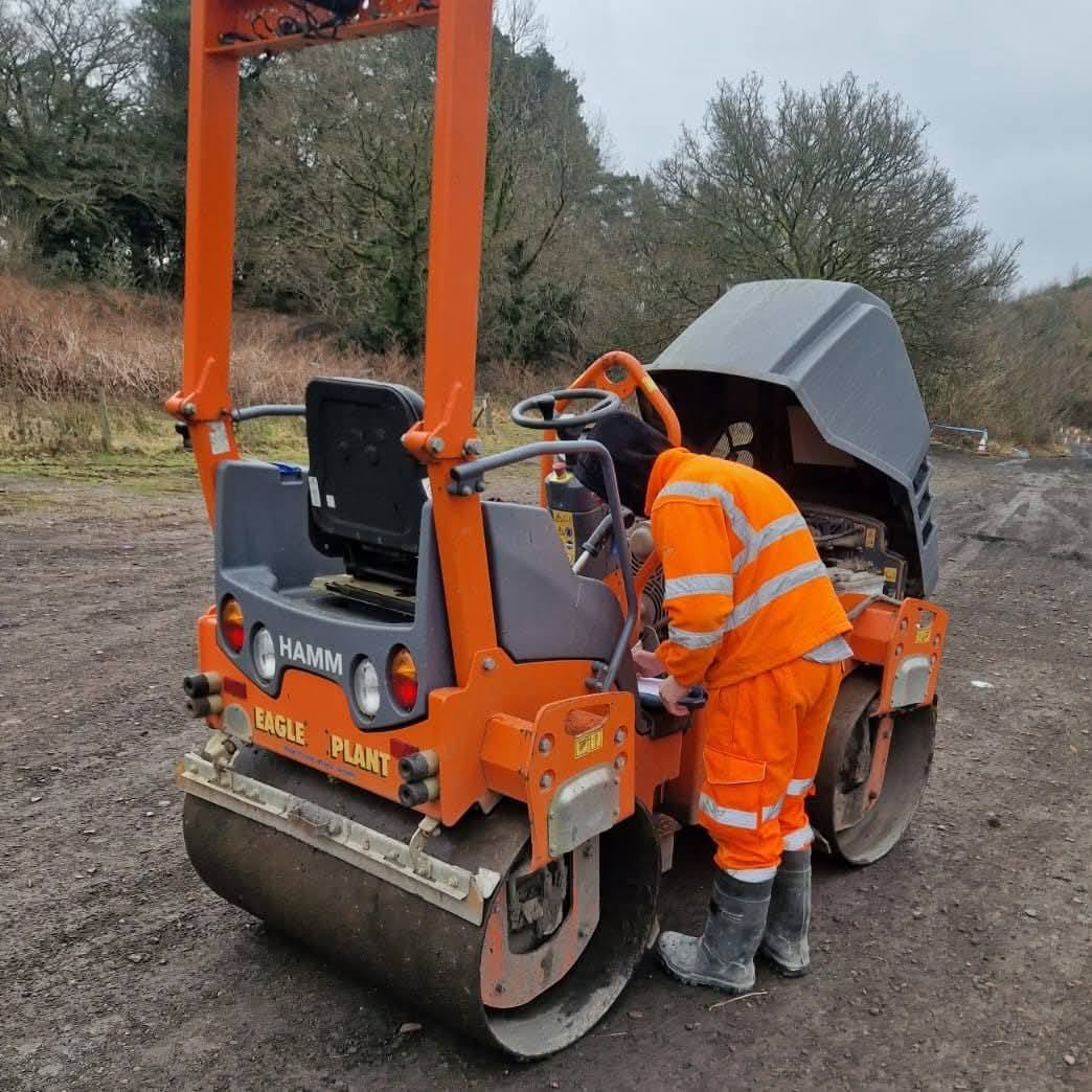 Operator carrying out a pre-use safety check on a road roller
